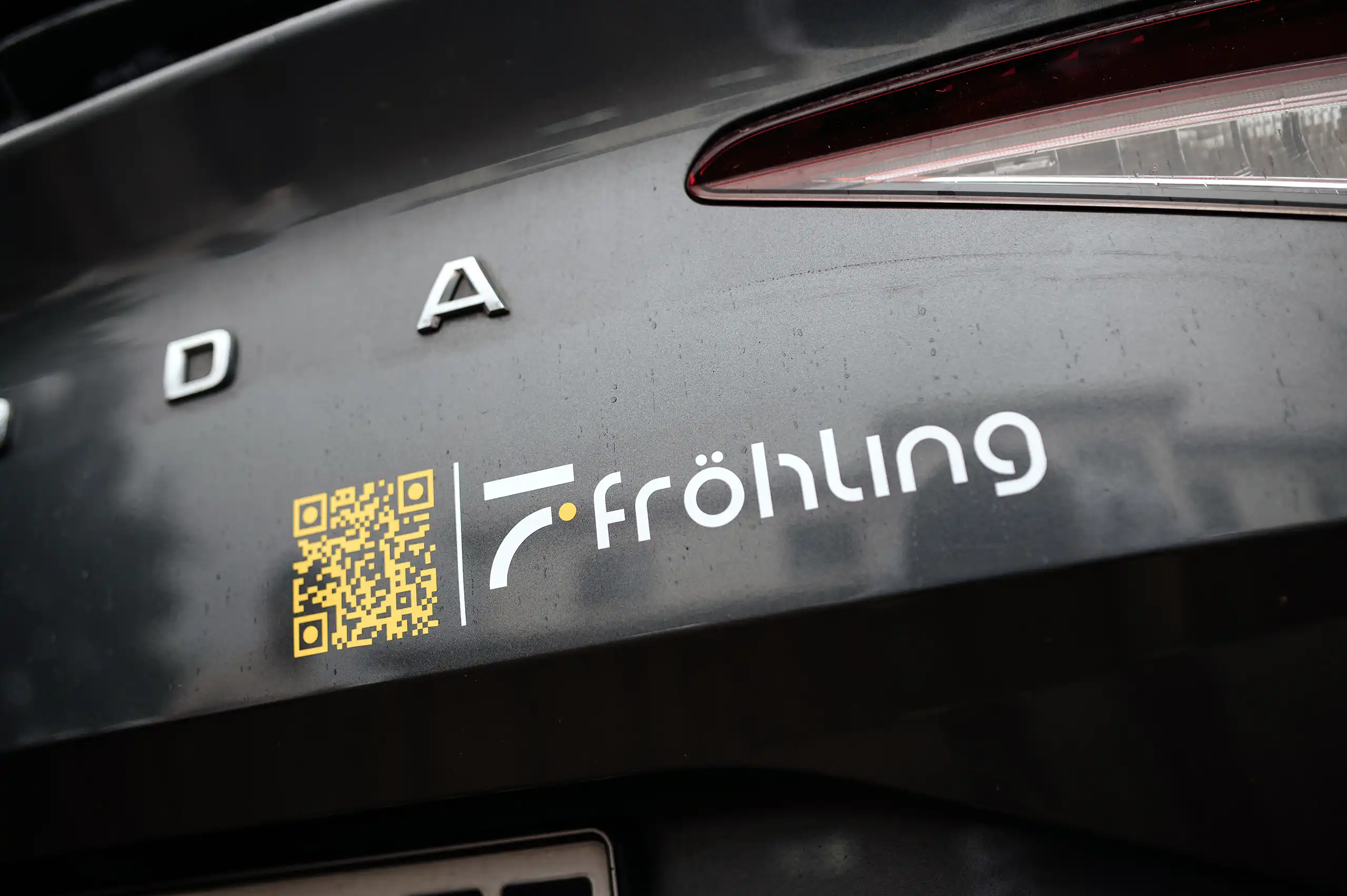 Heckansicht des Dienstfahrzeugs von Fröhling Ingenieure GmbH mit gelbem QR-Code und weißem Firmenlogo auf dunklem Fahrzeuglack